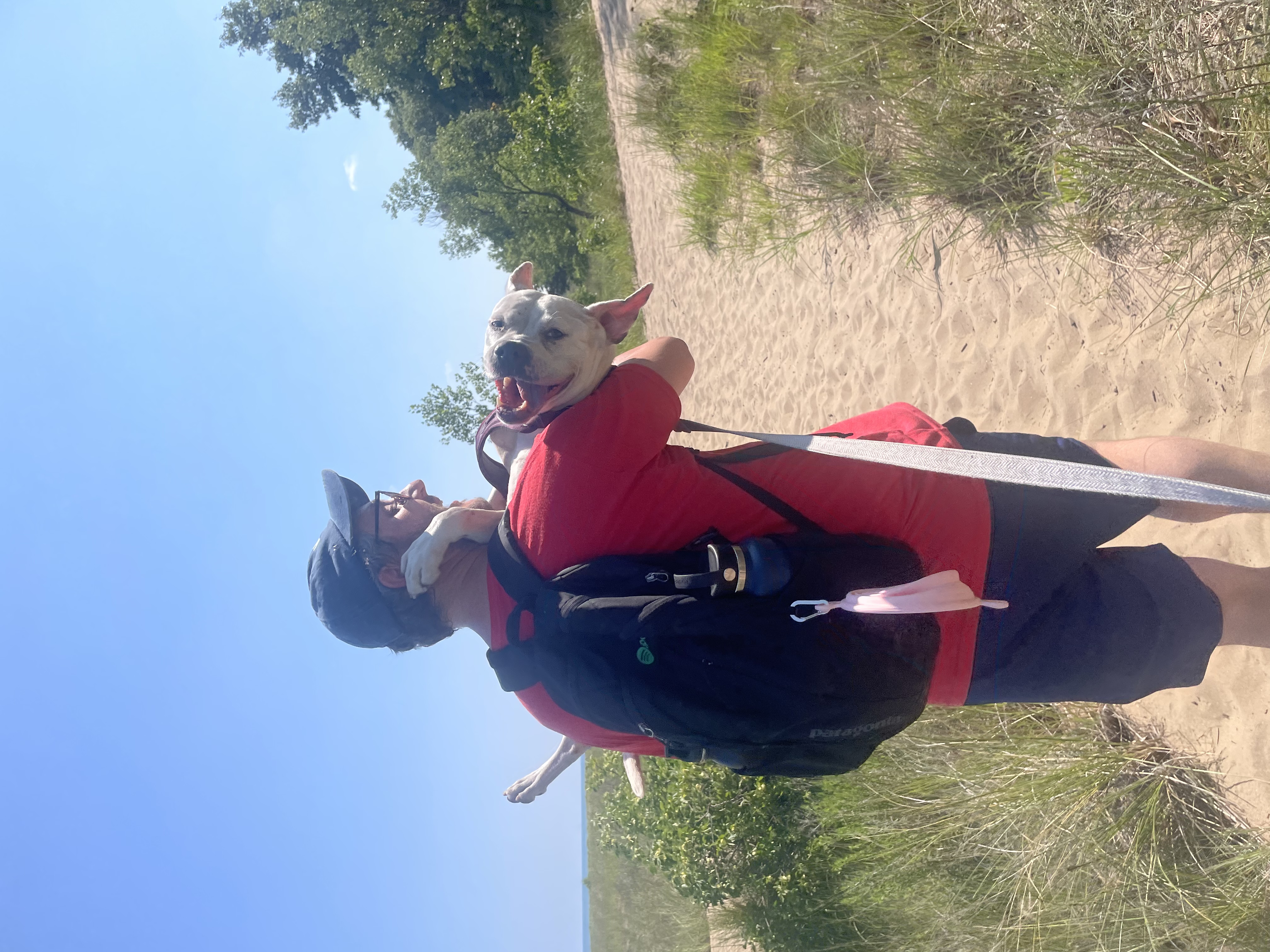 Peter carrying Mila on the beach on a hot, summer day. Mila is smiling without a care in the world.